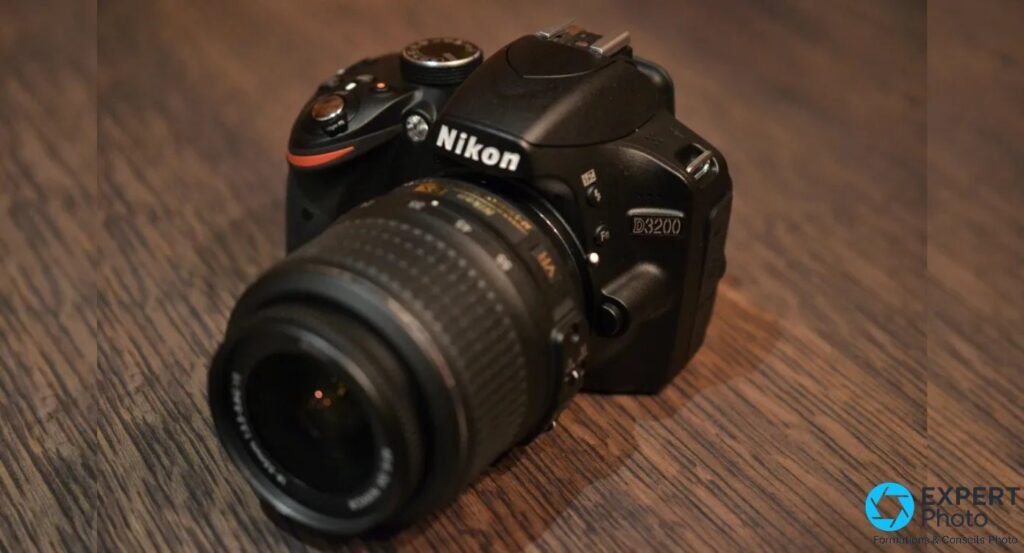  Nikon D3200 noir vu en plongée trois quarts haute, objectif 18-55mm Nikkor monté, table en bois clair