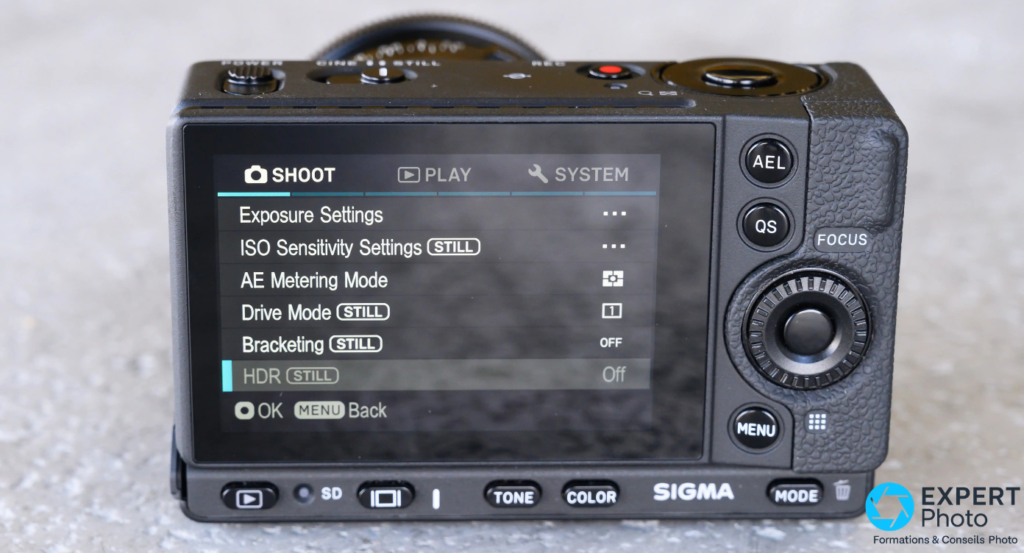Dos du Sigma fp avec menu SYSTEM à l'écran — boutons AEL, QS, molette de navigation et accès FOCUS