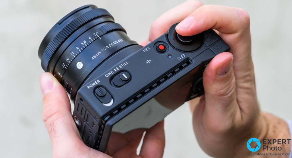 Sigma fp tenu en main, écran Quick Set affiché — réglages ISO 100, DNG+JPEG, format 3:2 et balance des blancs AWB