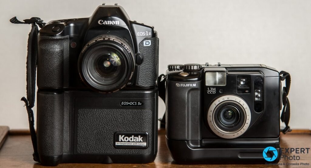 Canon EOS DCS-5c avec objectif EF 28-105mm aux côtés d'un compact Fujifilm 1.3M CCD, posés sur une table en bois