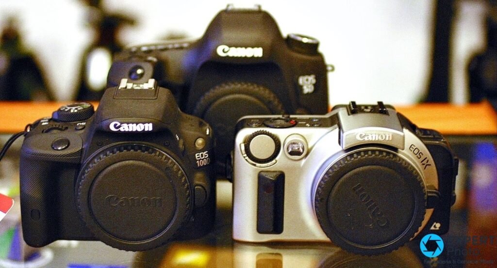 Trois boîtiers Canon face avant : EOS 100D noir à gauche, EOS 5D noir au fond, EOS IX argenté à droite sans objectif