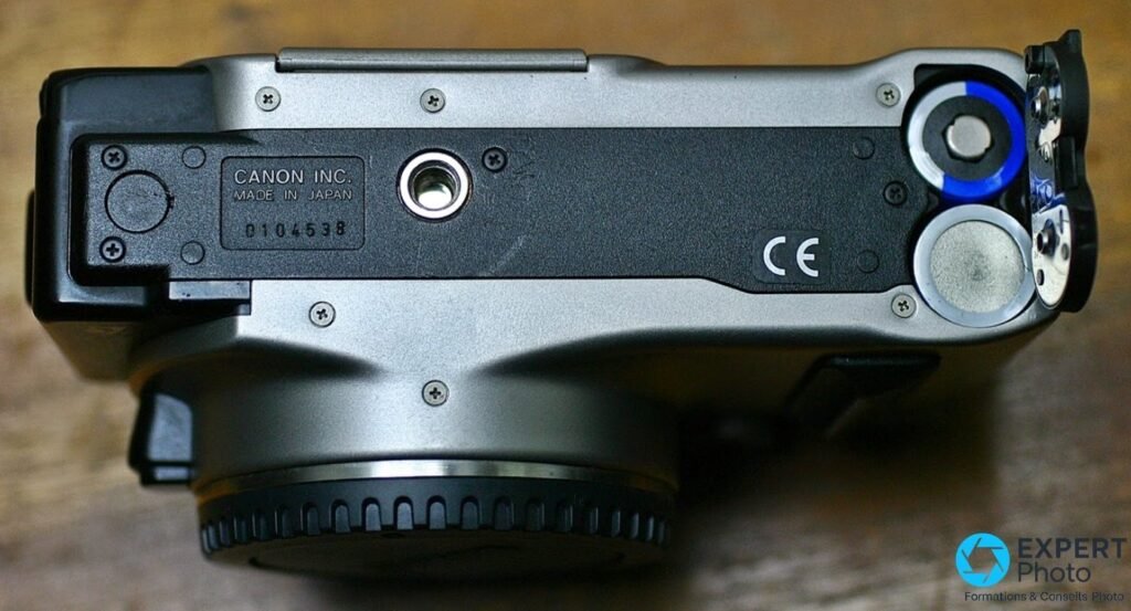 Canon EOS IX dessous, étiquette Made in Japan, filetage trépied, compartiment CR123A ouvert avec piles visibles