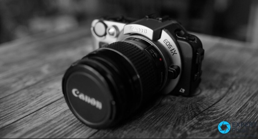 Canon EOS IX en noir et blanc, trois quarts avant, objectif Canon EF 28-80mm avec bouchon, logo EOS IX lisible