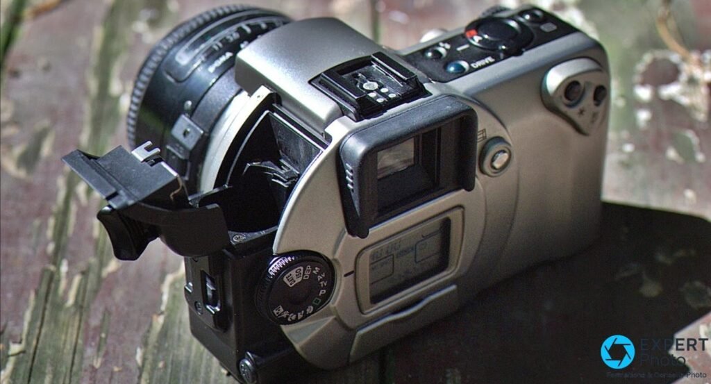 Canon EOS IX vu de trois quarts arrière, trappe APS ouverte, flash escamotable déployé, viseur et molette de modes visibles