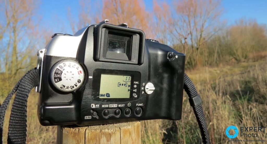 Canon EOS IX7 vu de dos : écran LCD allumé, molette modes (ISO, DATE/IX, scènes), viseur et touches MODE SELECT FUNC IX-RW