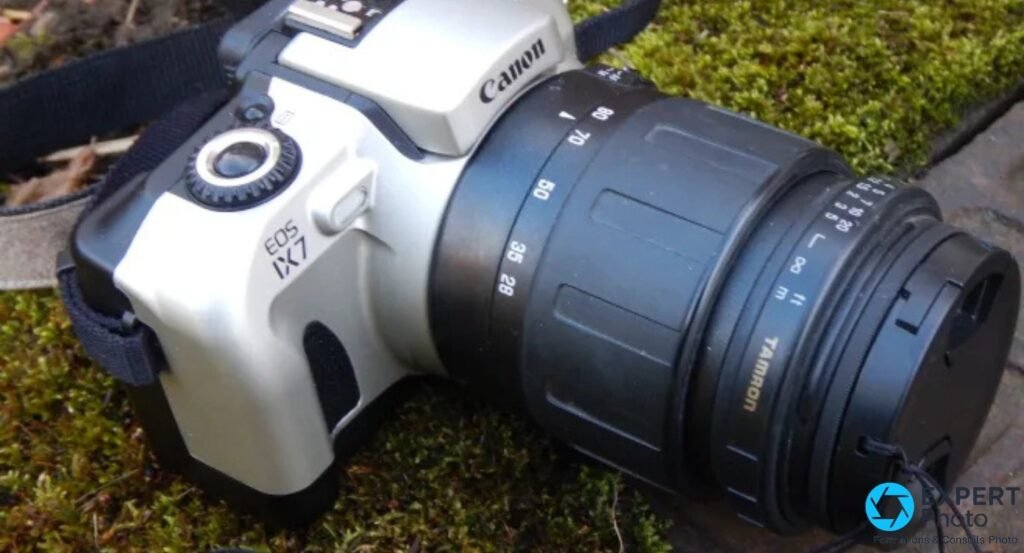 Canon EOS IX7 argentique APS, face gauche, objectif Tamron zoom monté, posé sur fond de mousse verte