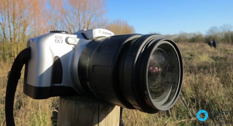 Canon EOS IX7 reflex APS argentique, trois quarts avant, objectif zoom asphérique monté, posé sur poteau bois en extérieur hivernal