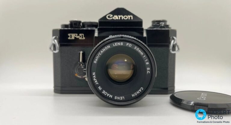 Test Canon F1N : mécanique solide, achat d’occasion à maîtriser Canon F-1 noir de face avec objectif Canon FD 50mm f/1.8 S.C. monté et bouchon d'objectif Canon posé à droite, fond blanc