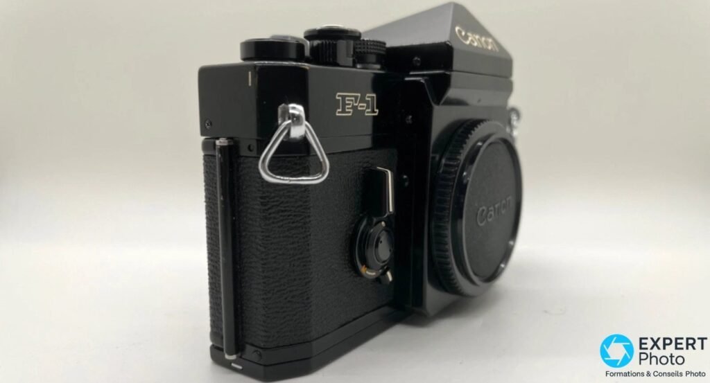 Canon F-1 de profil gauche : inscription F-1 dorée, leatherette texturée, anneau de sangle chromé et bouchon arrière monté