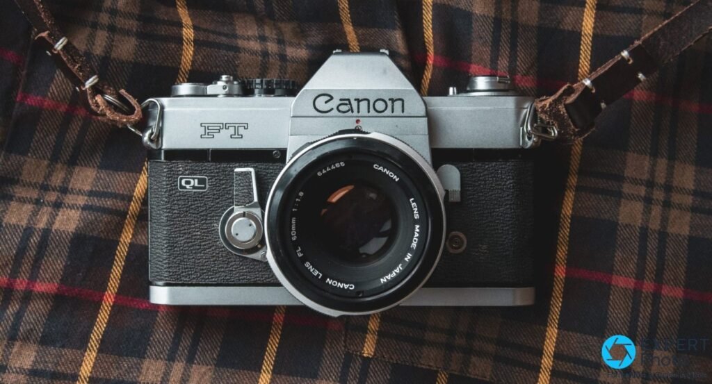 Canon FT QL posé de face sur tissu tartan brun-rouge avec sangle en cuir marron, objectif FL 50mm f/1.8 monté.