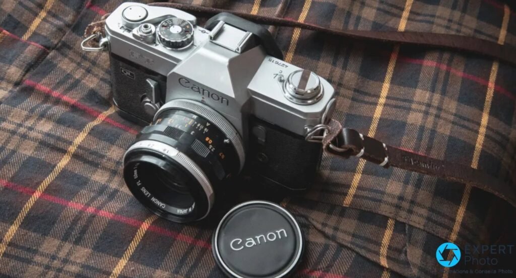 Canon FT QL posé en trois-quarts sur tissu tartan, capuchon Canon FL devant le boîtier, sangle cuir marron. 