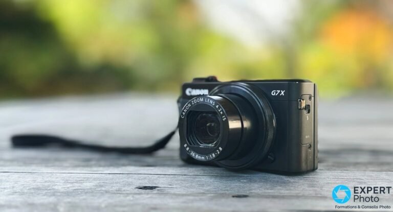 Canon PowerShot G7 X Mark II noir posé sur planches en bois, vue trois quarts, objectif sorti, fond bokeh vert flou