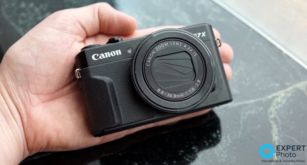 Canon PowerShot G7 X Mark II noir tenu dans une main, face avant avec objectif Canon Zoom Lens 4.2x IS 8.8-36.8mm fermé