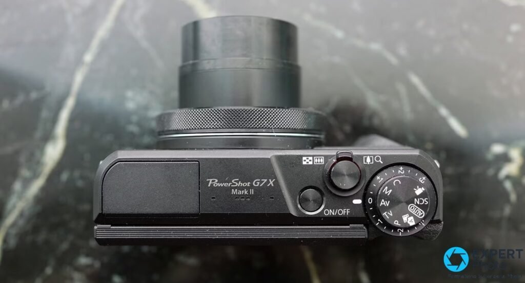 Canon PowerShot G7 X Mark II vu du dessus, molette modes M-Av-Tv-P-Auto, bouton ON/OFF et zoom sorti, fond marbre