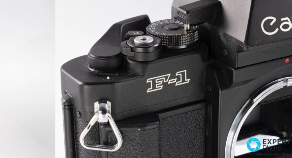  Gros plan Canon New F-1, marquage F-1 sur le corps noir, déclencheur fileté, anneau de courroie chromé visible côté gauche