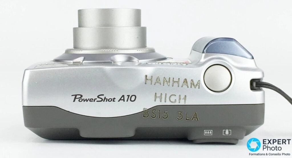 Canon PowerShot A10 vue de dessus, objectif sorti, corps gravé HANHAM HIGH BS15 3LA, déclencheur et bouton zoom visibles.
