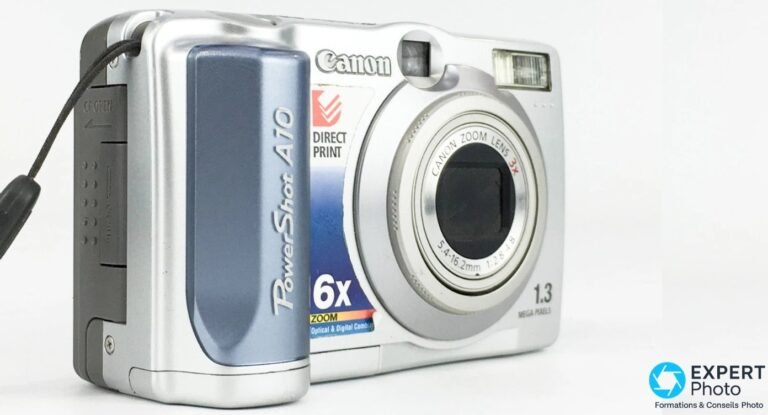 Canon PowerShot A10 vu trois quarts avant gauche, corps argent et bleu, sangle, objectif Canon Zoom Lens 3x, fond blanc.