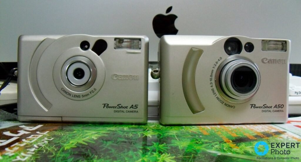 Canon PowerShot A5 posé sur bois en légère plongée, objectif 5mm F2.5 et flash visibles, lumière naturelle chaude