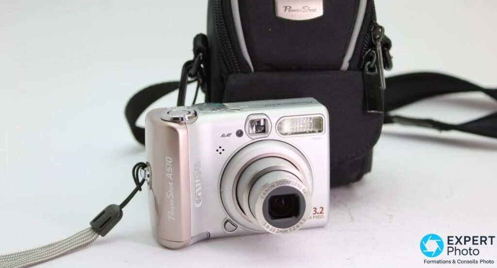 Canon PowerShot A510 face avant avec étui PowerShot noir en arrière-plan, objectif zoom 4x 3.2 Mpx et flash intégré visibles