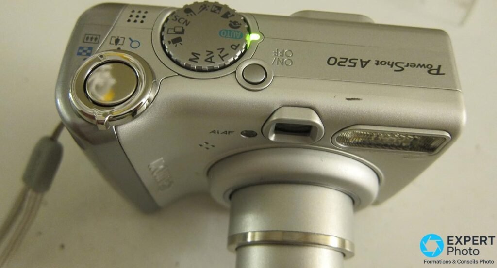 Canon PowerShot A520 vu du dessus, molette modes AUTO P AV TV M SCN, déclencheur et bouton ON/OFF, objectif déployé en bas