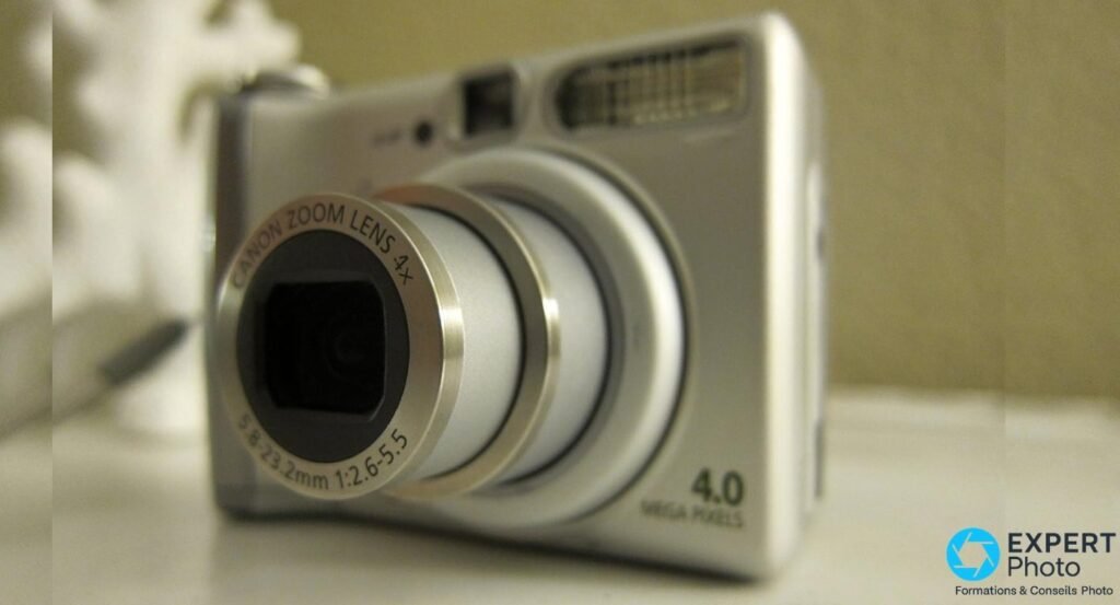 Canon PowerShot A520, gros plan objectif zoom 4x déployé, inscription 5.8-23.2mm 1:2.6-5.5, flash visible au second plan 