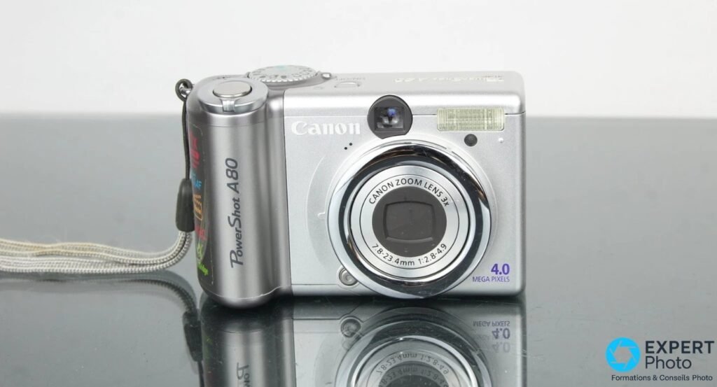 Canon PowerShot A80 face avant, objectif Canon Zoom Lens 3x centré, mention 4.0 Mega Pixels, flash intégré, fond gris