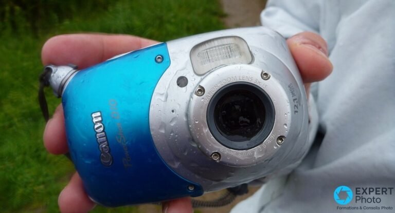 Canon PowerShot D10 tenu en main à l'extérieur, boîtier couvert de gouttes d'eau, objectif et flash visibles