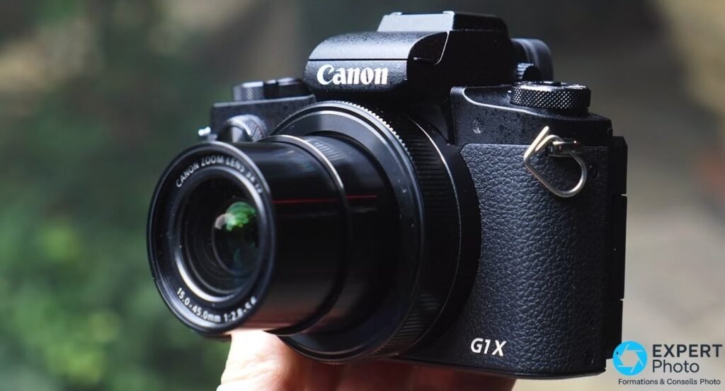 Canon PowerShot G1 X Mark III tenu en main, angle trois quarts avant, objectif 15-45mm f/2.8-5.6 sorti, logo G1X visible 