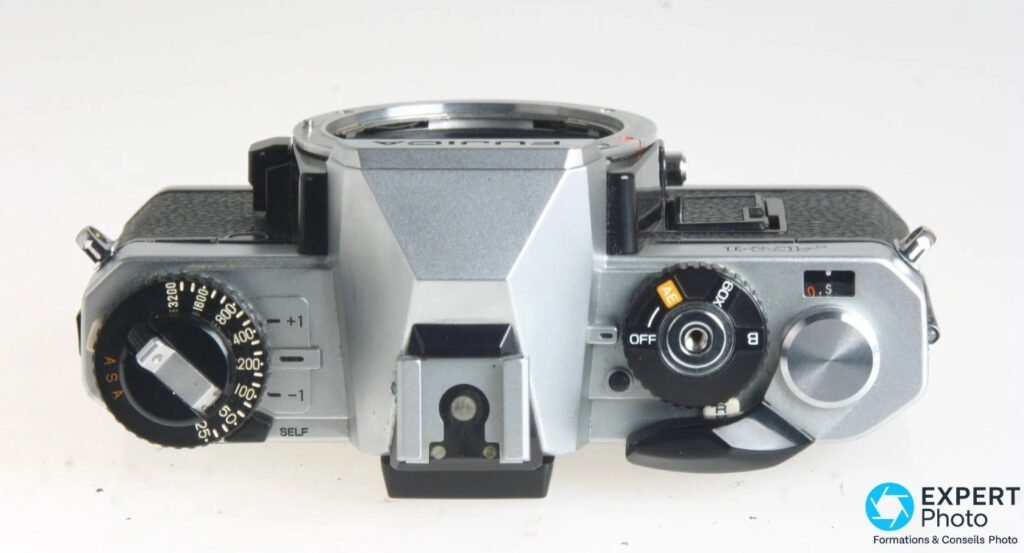 Fujica AX-1 vu du dessus : molette ASA, sélecteur de mode AE/60X/B/OFF orange, déclencheur et griffe flash