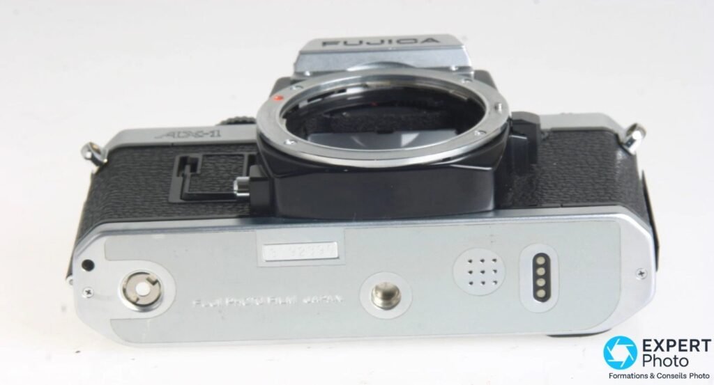 Fujica AX-1 vu de dessous : semelle chromée, pas de vis trépied, connecteurs et inscription AX-1