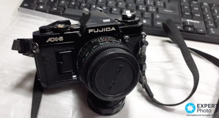 Fujica AX-5 noir de face, inscriptions FUJICA et AX-5 visibles, objectif X-Fujinon avec capuchon, sangle noire