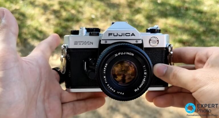 Fujica STX-1N face avant, objectif X-Fujinon 50mm f/1.9 centré, inscriptions STX-1N et FUJICA lisibles, fond herbe flou