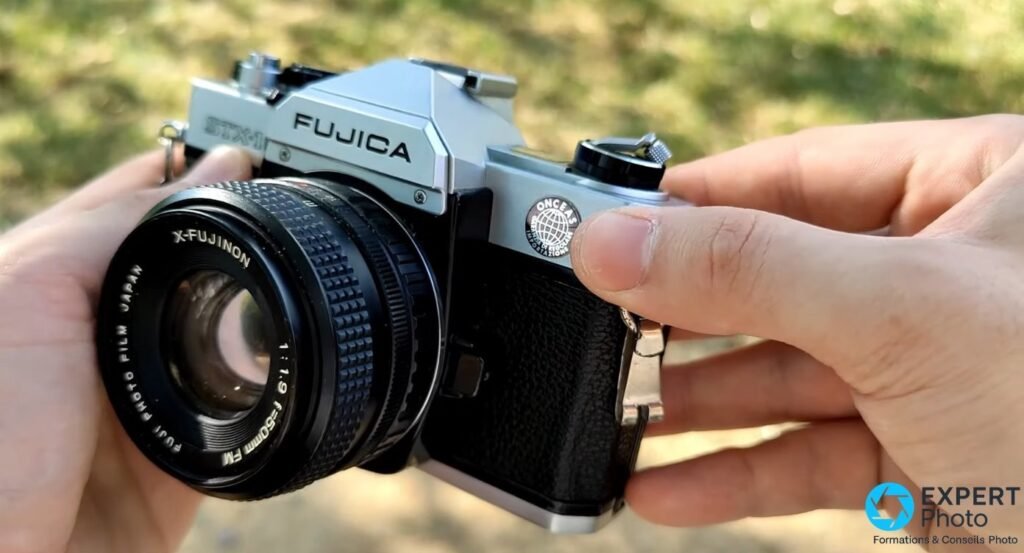 Fujica STX-1N tenu en mains, vue trois quarts avant, objectif X-Fujinon 50mm f/1.9 monté, inscription FUJICA visible