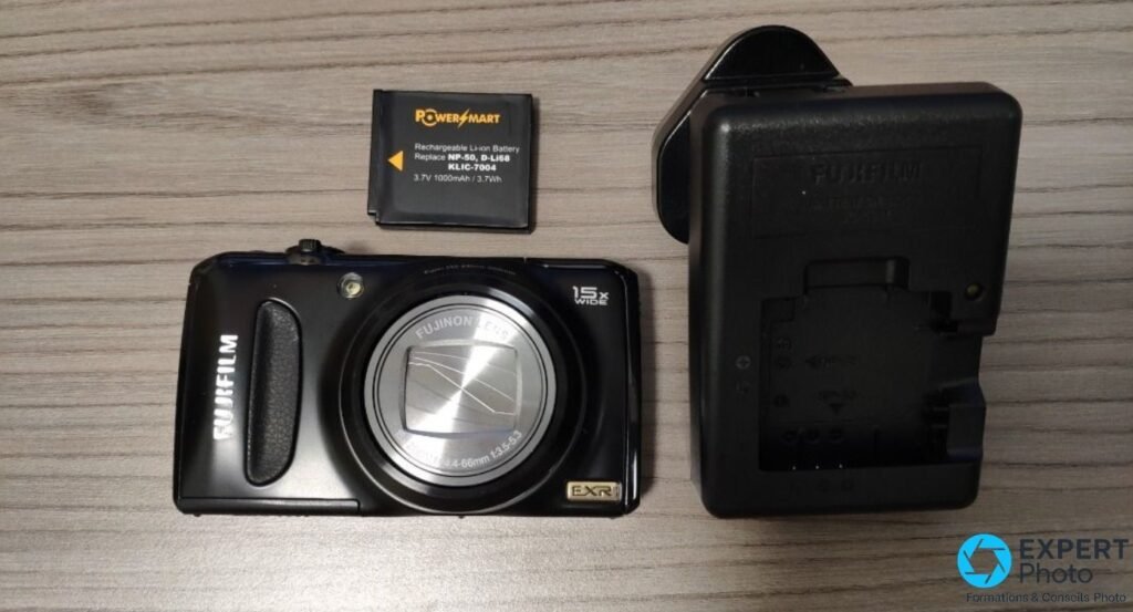 Fujifilm F300EXR face avant, posé à côté d'une batterie NP-50 PowerSmart et d'un chargeur Fujifilm, sur fond bois