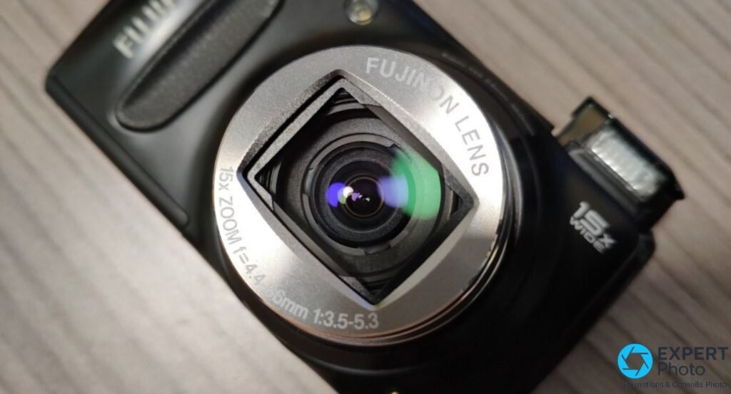 Gros plan sur l'objectif Fujinon du Fujifilm F300EXR zoom déployé, inscription 15x f=4.4-66mm et reflet bleu-vert