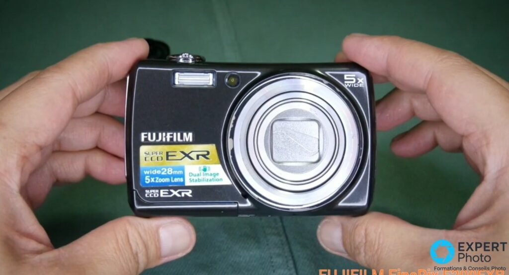Fujifilm FinePix F200EXR face avant tenu en mains, flash ouvert, objectif fermé, logo Super CCD EXR et 5x Zoom Lens visibles.