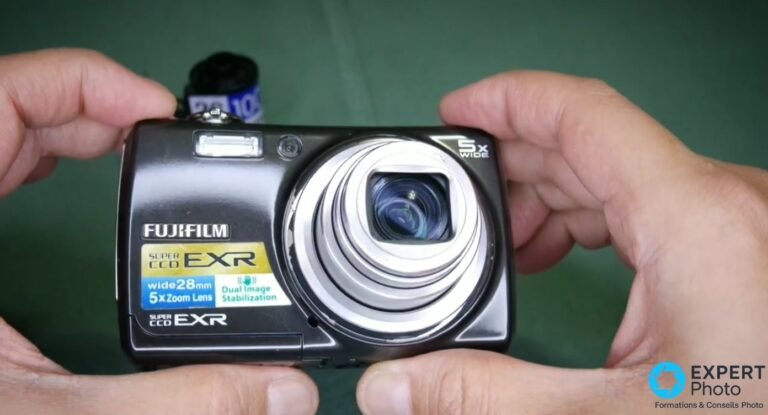 Fujifilm FinePix F200EXR face avant tenu en mains, objectif déployé, badge Super CCD EXR et mentions 28 mm, stabilisation.