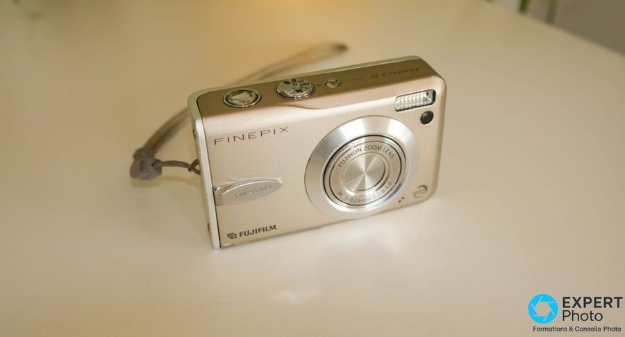 Fujifilm FinePix F30 compact argenté posé sur une surface blanche, volet objectif fermé, logo FinePix et Fujifilm visibles 