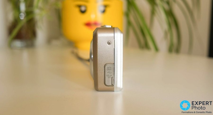 Fujifilm FinePix F30 profil droit, trappe ouverte révélant les ports AV Out, USB mini et DC In 5V pour chargeur externe