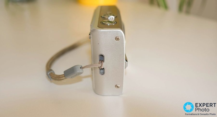 Fujifilm FinePix F30 profil gauche, dragonne grise FinePix attachée, port mini-USB visible sur la tranche du boîtier compact