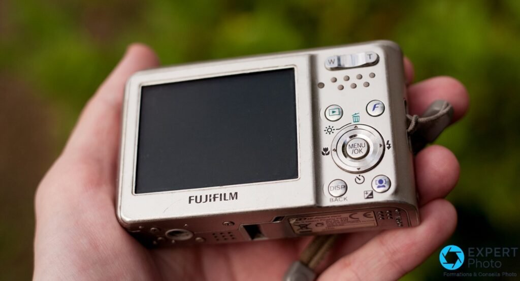 Fujifilm FinePix F31fd tenu en main, dos avec écran LCD éteint, touches MENU/OK, DISP/BACK, molette zoom W/T