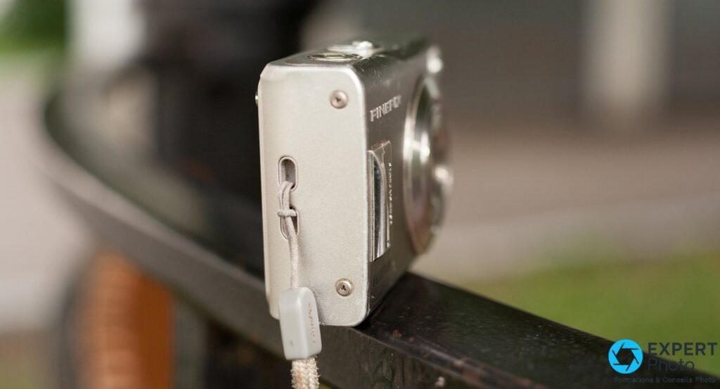 Fujifilm FinePix F31fd vu de côté droit posé sur rambarde, passant de dragonne avec lanière grise d'origine attachée