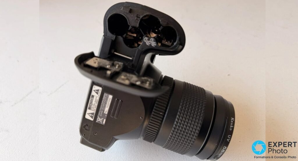 Fujifilm FinePix S6500fd retourné, trappe du compartiment 4 piles AA ouverte avec filtre Kenko UV 58 mm visible 