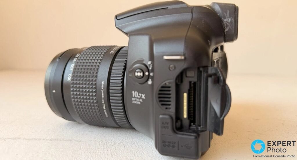 Profil gauche du Fujifilm FinePix S6500fd, bague crantée 10,7x, trappe USB et A/V ouverte sur le flanc