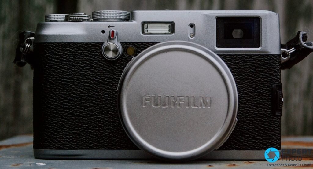 Fujifilm FinePix X100 vu de face, bouchon d'objectif avec logo Fujifilm, molettes vitesse et correction d'exposition