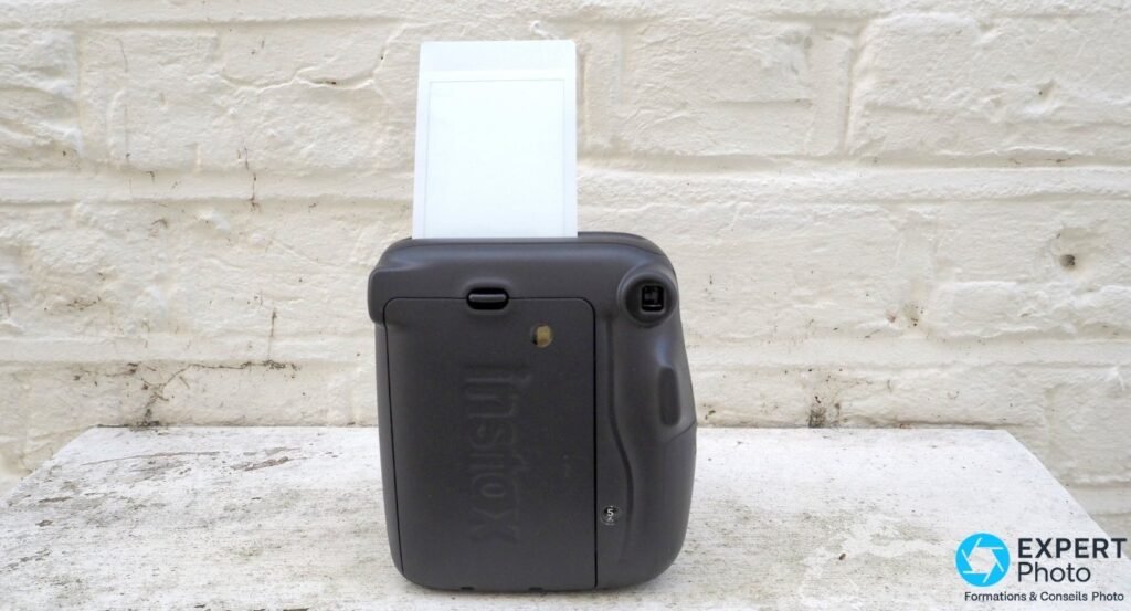 Fujifilm Instax Mini 11 noir vu de dos, tirage Instax mini en cours de sortie par la fente supérieure