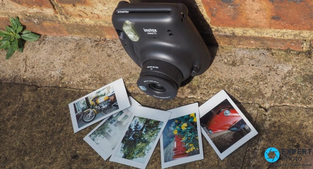 Fujifilm Instax Mini 11 noir vu en plongée avec cinq tirages Instax mini développés posés au sol