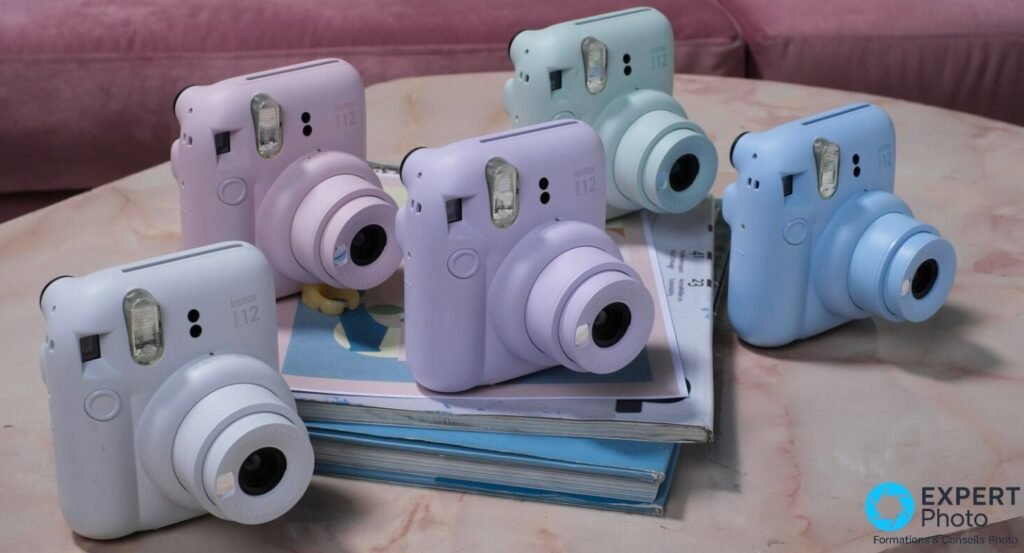 Cinq Fujifilm Instax Mini 12 de couleurs pastel — vert, rose, violet, bleu et bleu clair — posés sur une table en marbre