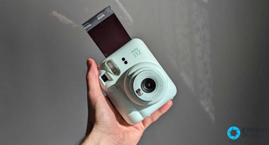 Fujifilm Instax Mini 12 vert menthe tenu en main avec un tirage Instax Mini en cours d'éjection par le haut du boîtier