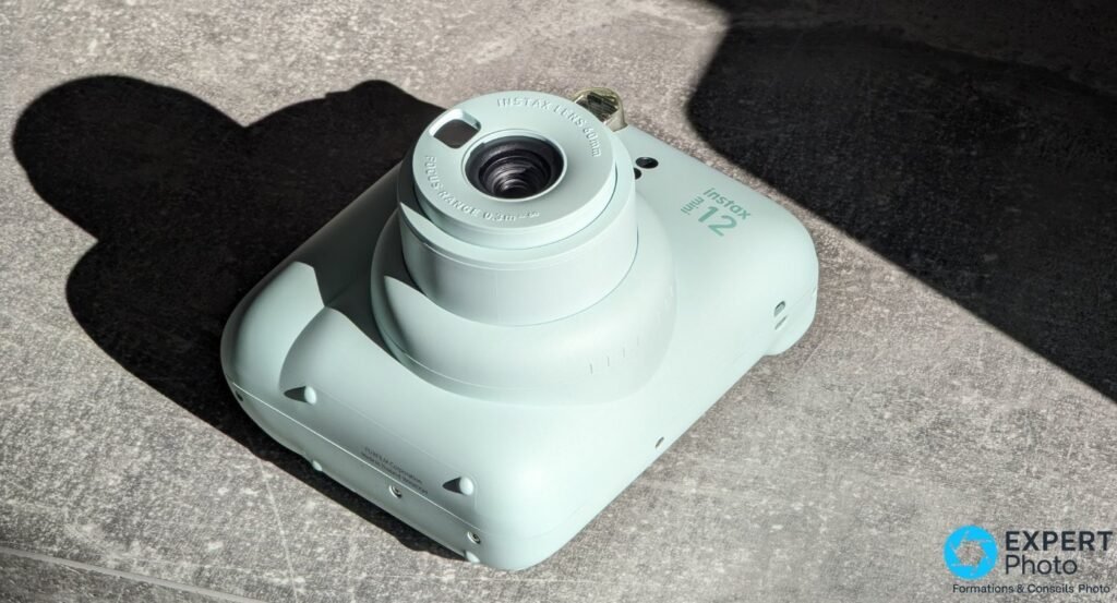 Fujifilm Instax Mini 12 vert menthe vu de dessus en plongée, objectif déployé avec marquage Instax Lens 60mm et focus range